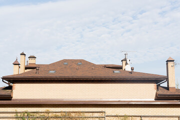 Naklejka premium modern residential brick house with a detailed view of its roof featuring multiple chimneys, skylights, and a clear blue sky in the background