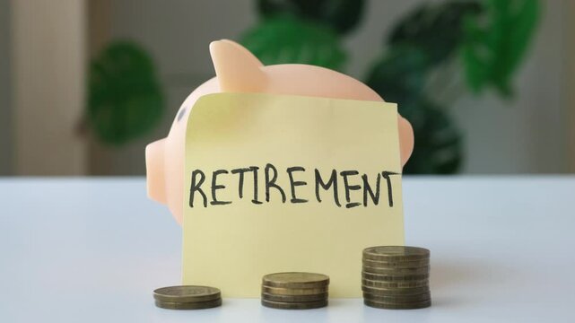 Hand putting coins into piggy bank with paper label Retirement. Saving money for pension concept