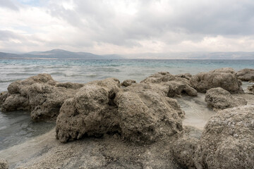 Turquoise waters and white mineral beaches of Lake Salda, Turkey, with a cloudy sky and rocky formations in the background.