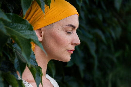 Young female cancer patient wearing headscarf closed eyes side view garden portrait. Mental wellbeing, emotional support, contemplation and mindfulness during cancer illness.