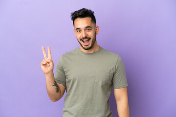 Fototapeta premium Young caucasian man isolated on purple background smiling and showing victory sign