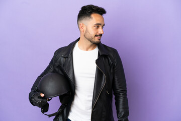 Fototapeta premium Young man with a motorcycle helmet isolated on purple background looking side