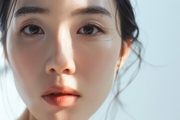 Fototapeta premium Close-up of a young woman with a soft, radiant complexion, gazing directly at the camera with a slightly inquisitive expression.