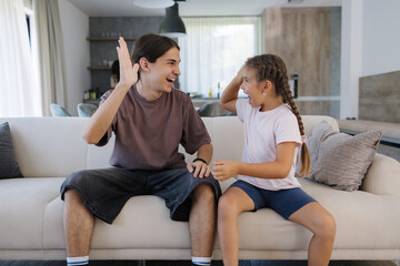 Obraz premium Teenage brother gave high five to his six year old sister after they finish and win game on console. 