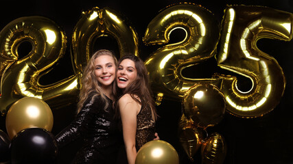 Happy gorgeous girls in stylish sexy party dresses holding gold 2025 balloons, having fun at New...