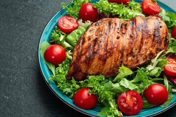 Grilled chicken breast ( fillet ) with lattuce salad and cherry tomatoes . Top view