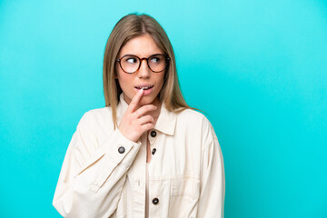 Young caucasian woman isolated on blue background With glasses and having doubts