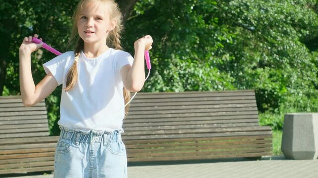Preteen girl with jumping rope in park. Portrait of happy caucasian kid jumping with skipping rope outdoors in summer park