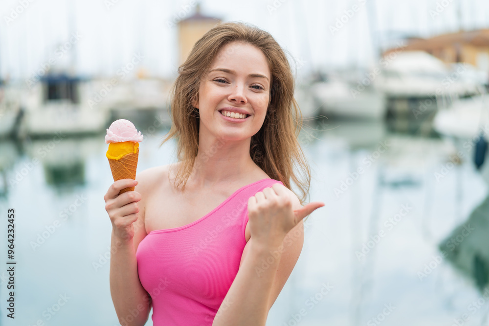 Poster Young redhead woman with a cornet ice cream at outdoors pointing to the side to present a product