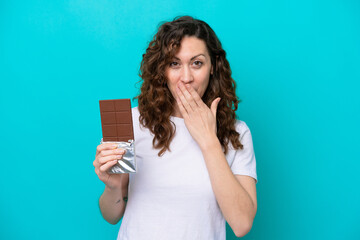 Young caucasian woman isolated on blue background taking a chocolate tablet and surprised