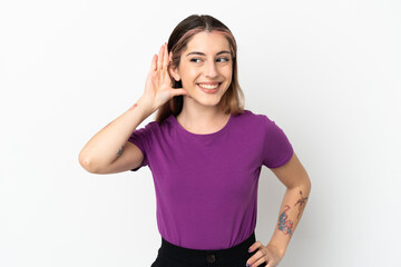 Young caucasian woman isolated on white background listening to something by putting hand on the ear