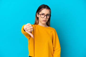 Young caucasian woman isolated on blue background showing thumb down with negative expression