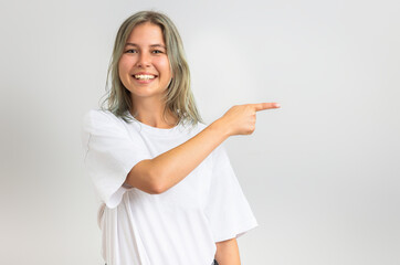 Cheerful young woman pointing finger at blank copy space. Isolated on grey background.