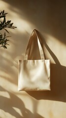 A beige tote bag hangs on a textured wall with soft shadows and sunlight, embodying minimalist style and eco-conscious fashion.
