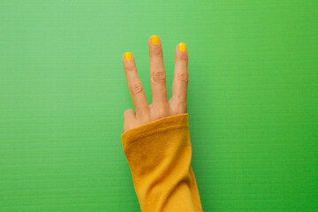 Three fingers of a woman with her nails painted yellow on a green background.