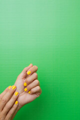 A woman's hands with her nails painted yellow on a green background.