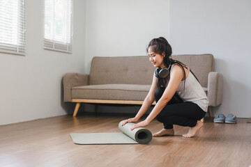 Asian Woman rolling exercise mat in living room. Yoga at home active lifestyle concept