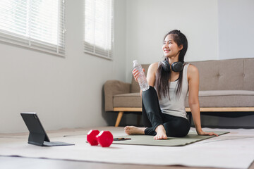 Young Asian woman at home doing exercise in front of open laptop, repeating instructions by...