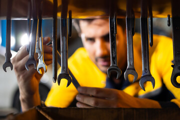 Auto mechanic selecting tools and spanner for repairs in auto repair shop. Hispanic latin male mechanic repairs car in garage. Car maintenance and auto service garage concept