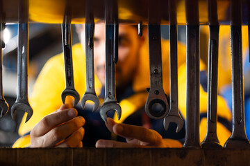 Auto mechanic selecting tools and spanner for repairs in auto repair shop. Hispanic latin male mechanic repairs car in garage. Car maintenance and auto service garage concept
