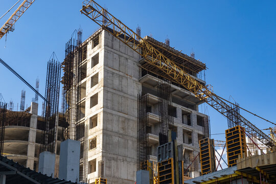 Scenery with buildings under construction. Crane boom over construction site. Erection of multi-storey buildings. Process of building houses with residential apartments. Erection monolithic buildings