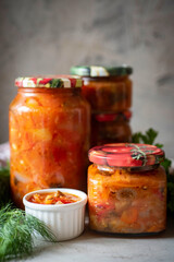 Pickled vegetables in tomato sauce in a glass jar on a gray background.Close-up. Vertical photo