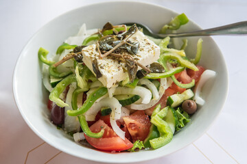 Traditional Greek salad in Rhodes, Greece. Greek salad is made with pieces of tomatoes, cucumbers, onion, feta cheese, and olives and dressed with salt, Greek oregano, lemon juice and olive oil.