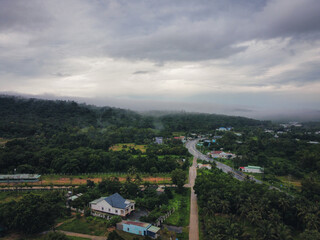 Aerial shot in the outskirts of Le Bat, Phu Quoc, Vietnam. A small town can be seen, surrounded with rainforest with a road cutting through the middle. Traditional wooden houses can be seen