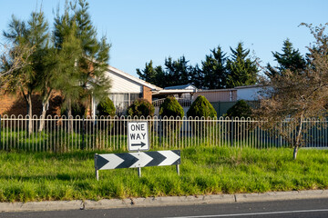 Sign indicating a one-way street on a suburban road in Australia with a residential home in the...