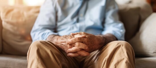 Close-up of a man's hands clasped together while sitting on a sofa