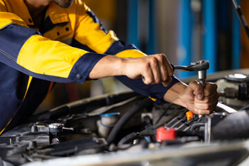 Obraz premium Close up mechanical hand with tools and spanner. Hispanic latin male mechanic repairs car in garage. Car maintenance and auto service garage concept
