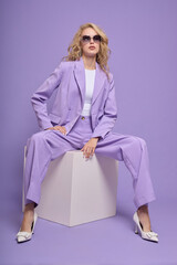 Fashion female model in lilac suit, white shoes, top and sunglasses.