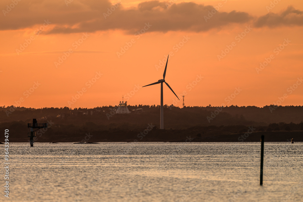 Wall mural wind power turbine with an old airport tower in the background at sunset.