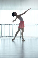 Fototapeta premium Teenage ballerina practices ballet in a pink outfit in a studio