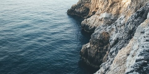 A serene view of rocky cliffs meeting calm ocean waters under soft natural light.