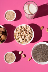 Semillas de chía, sésamo, nueces, pistachos y un vaso de leche vegetal. Frutos secos sobre un fondo rosa. Vista superior