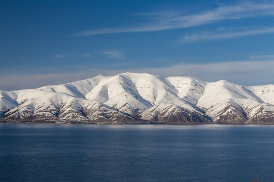 snow capped mountains on lake sevan in clear weather at sunset