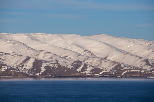 snow capped mountains on lake sevan in clear weather at sunset