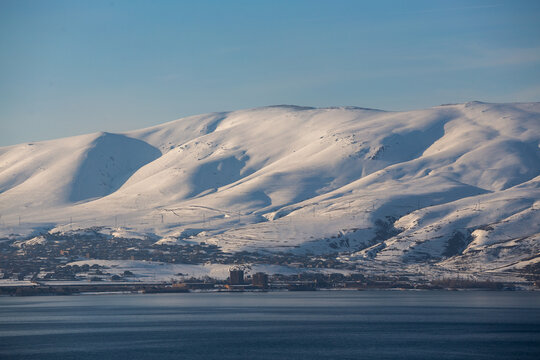 snow capped mountains on lake sevan in clear weather at sunset