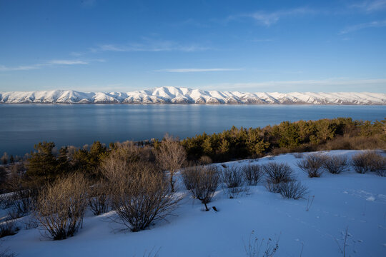 snow capped mountains on lake sevan in clear weather at sunset