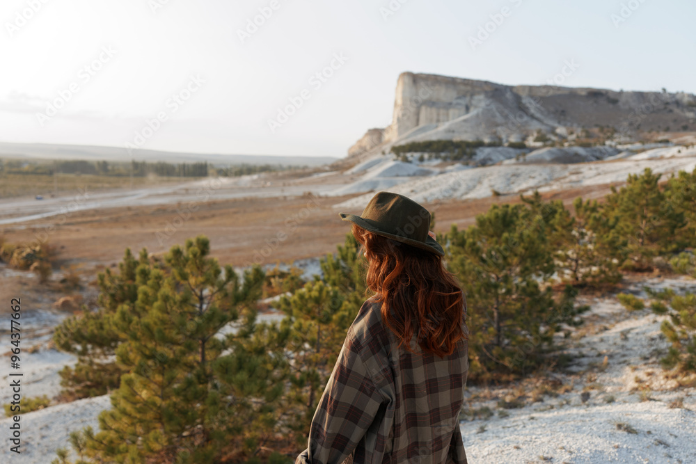 Wall mural Outdoor adventure woman in plaid shirt and hat standing in front of majestic rock formation