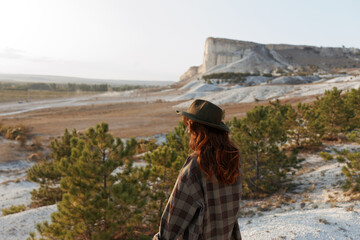 Outdoor adventure woman in plaid shirt and hat standing in front of majestic rock formation © VICHIZH
