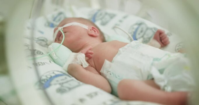 Little boy in incubator with breathing tube, selective focus on baby. Neonatal intensive care unit for premature babies. Premature newborn baby boy in hospital incubator after c-section