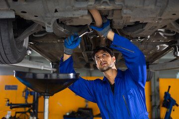 Under car. hispanic latin male mechanic repairs car in garage. Closeup hand. Auto car mechanic checking the oil level of the car engine. Car repair and maintenance