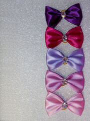 Pink, purple, fuchsia and indigo bows with a stone in the middle lie on a gray shiny background. many bright beautiful bows. pet accessories. top view. five bows, copy space