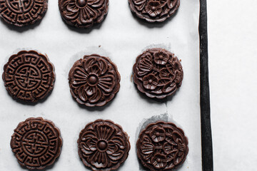 Overhead view of stamped chocolate cookies on a parchment lined baking tray, top view of embossed chocolate sugar cookies on a white background