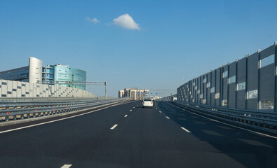 Expressway under blue sky. Highway in modern city. Three-lane new road. Highway with soundproof shields. Modern bridge in sunny metropolis. Expressway near high-rise residential buildings