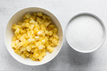 Overhead view of diced pineapple and sugar in white bowls, process of making pineapple cheong or...