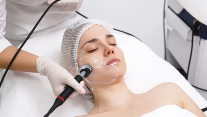 A cosmetologist applies radiofrequency lifting to a young woman in a modern clinic. This advanced...