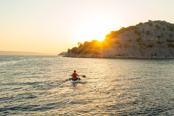 Man in orange vest navigating on the paddleboard in the sea at sunset.